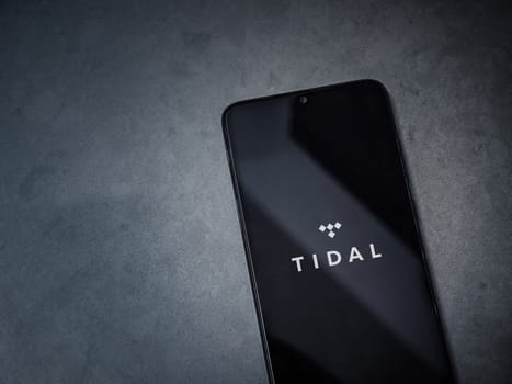 Lod, Israel - July 16,2023: TIDAL Music app launch screen on smartphone on dark marble stone background. Top view flat lay with copy space.
