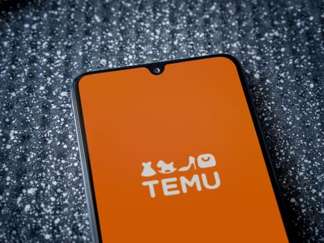 Lod, Israel - July 16,2023: Temu app launch screen on smartphone on metallic background. Close up top view flat lay.