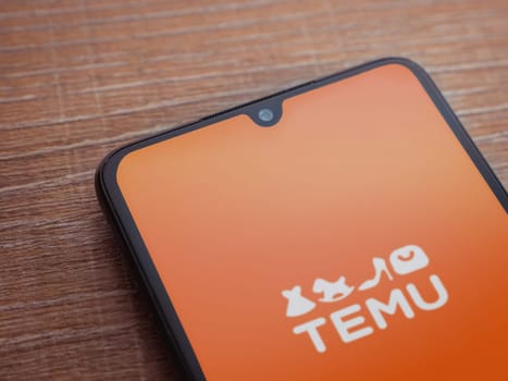 Lod, Israel - July 16,2023: Temu app launch screen on smartphone on wooden background. Top view flat lay with copy space.