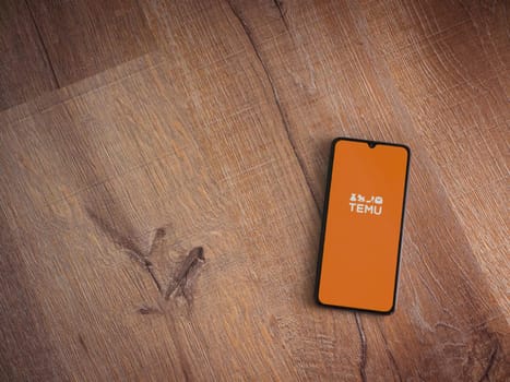 Lod, Israel - July 16,2023: Temu app launch screen on smartphone on wooden background. Top view flat lay with copy space.