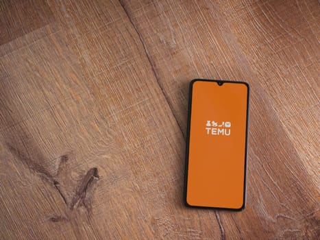 Lod, Israel - July 16,2023: Temu app launch screen on smartphone on wooden background. Top view flat lay with copy space.