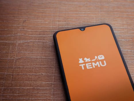 Lod, Israel - July 16,2023: Temu app launch screen on smartphone on wooden background. Top view flat lay with copy space.