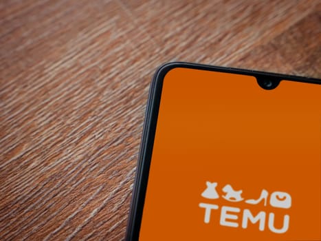 Lod, Israel - July 16,2023: Temu app launch screen on smartphone on wooden background. Top view flat lay with copy space.