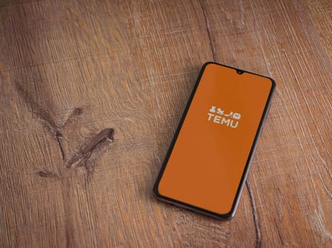 Lod, Israel - July 16,2023: Temu app launch screen on smartphone on wooden background. Top view flat lay with copy space.
