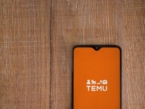 Lod, Israel - July 16,2023: Temu app launch screen on smartphone on wooden background. Top view flat lay with copy space.