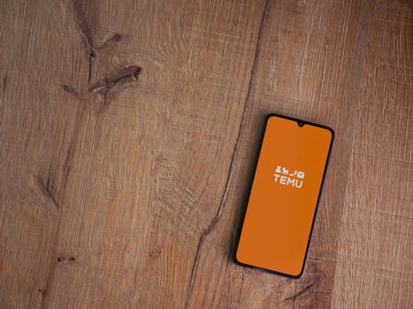 Lod, Israel - July 16,2023: Temu app launch screen on smartphone on wooden background. Top view flat lay with copy space.