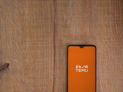 Lod, Israel - July 16,2023: Temu app launch screen on smartphone on wooden background. Top view flat lay with copy space.