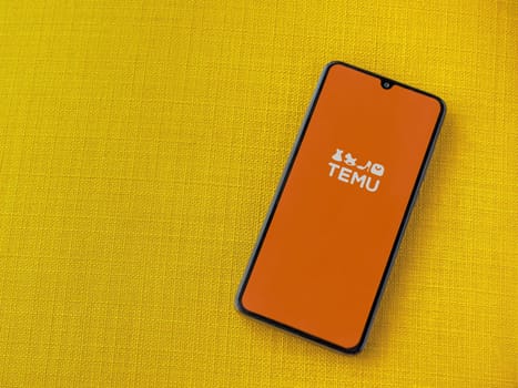 Lod, Israel - July 16,2023: Temu app launch screen on smartphone on yellow fabric background. Top view flat lay with copy space.