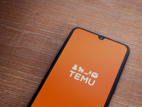 Lod, Israel - July 16,2023: Temu app launch screen on smartphone on wooden background. Top view flat lay with copy space.
