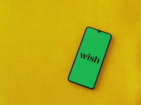 Lod, Israel - July 16,2023: Wish app launch screen on smartphone on yellow fabric background. Top view flat lay with copy space.