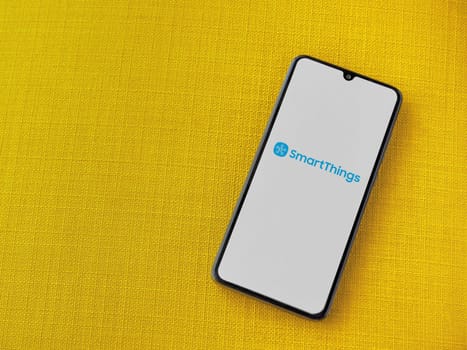 Lod, Israel - July 16,2023: Smartthings app launch screen on smartphone on yellow fabric background. Top view flat lay with copy space.