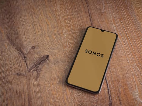 Lod, Israel - July 16,2023: Sonos app launch screen on smartphone on wooden background. Top view flat lay with copy space.