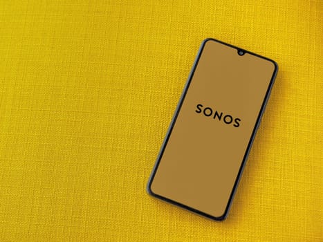 Lod, Israel - July 16,2023: Sonos app launch screen on smartphone on yellow fabric background. Top view flat lay with copy space.