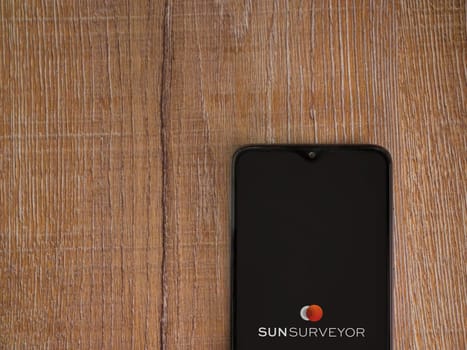 Lod, Israel - July 16,2023: Sun Surveyor app launch screen on smartphone on wooden background. Top view flat lay with copy space.