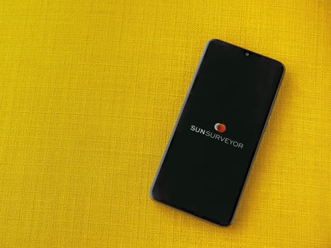 Lod, Israel - July 16,2023: Sun Surveyor app launch screen on smartphone on yellow fabric background. Top view flat lay with copy space.