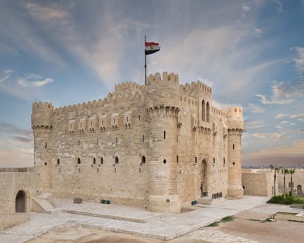 The Citadel of Qaitbay, a majestic 15th century castle in Alexandria, Egypt, against a vibrant sunset sky