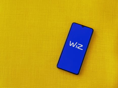 Lod, Israel - July 16,2023: WIZ app launch screen on smartphone on yellow fabric background. Top view flat lay with copy space.
