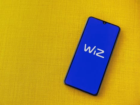Lod, Israel - July 16,2023: WIZ app launch screen on smartphone on yellow fabric background. Top view flat lay with copy space.