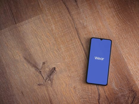 Lod, Israel - July 16,2023: Wear - Galaxy Wearable app launch screen on smartphone on wooden background. Top view flat lay with copy space.