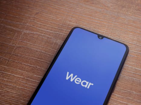 Lod, Israel - July 16,2023: Wear - Galaxy Wearable app launch screen on smartphone on wooden background. Top view flat lay with copy space.
