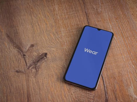 Lod, Israel - July 16,2023: Wear - Galaxy Wearable app launch screen on smartphone on wooden background. Top view flat lay with copy space.