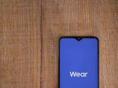 Lod, Israel - July 16,2023: Wear - Galaxy Wearable app launch screen on smartphone on wooden background. Top view flat lay with copy space.