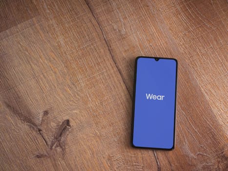 Lod, Israel - July 16,2023: Wear - Galaxy Wearable app launch screen on smartphone on wooden background. Top view flat lay with copy space.