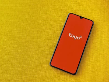 Lod, Israel - July 16,2023: Tuya Smart app launch screen on smartphone on yellow fabric background. Top view flat lay with copy space.