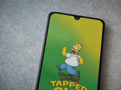Lod, Israel - July 16,2023: The Simpsons Tapped Out app launch screen on smartphone on ceramic stone background. Top view flat lay with copy space.