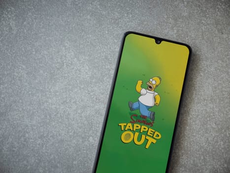 Lod, Israel - July 16,2023: The Simpsons Tapped Out app launch screen on smartphone on ceramic stone background. Top view flat lay with copy space.