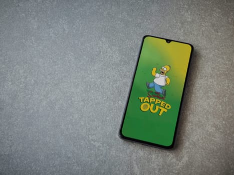 Lod, Israel - July 16,2023: The Simpsons Tapped Out app launch screen on smartphone on ceramic stone background. Top view flat lay with copy space.