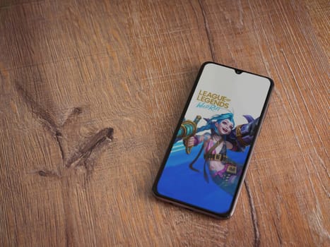 Lod, Israel - July 16,2023: League of Legends - Wild Rift app launch screen on smartphone on wooden background. Top view flat lay with copy space.