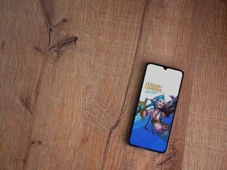 Lod, Israel - July 16,2023: League of Legends - Wild Rift app launch screen on smartphone on wooden background. Top view flat lay with copy space.