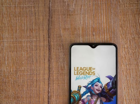 Lod, Israel - July 16,2023: League of Legends - Wild Rift app launch screen on smartphone on wooden background. Top view flat lay with copy space.