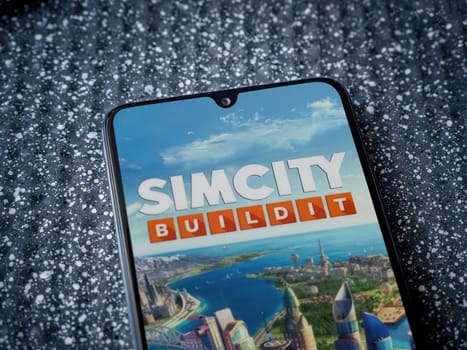 Lod, Israel - July 16,2023: SimCity BuildIt app launch screen on smartphone on metallic background. Close up top view flat lay.