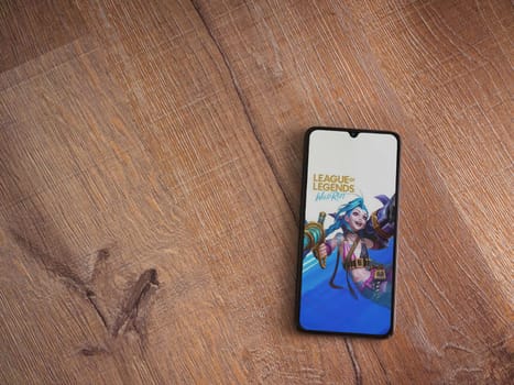 Lod, Israel - July 16,2023: League of Legends - Wild Rift app launch screen on smartphone on wooden background. Top view flat lay with copy space.
