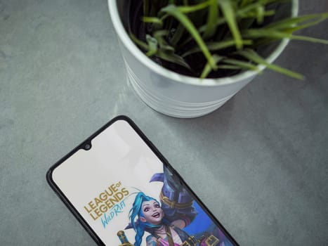 Lod, Israel - July 16,2023: Modern workspace with smartphone with League of Legends - Wild Rift app launch screen on marble background. Close up top view flat lay.
