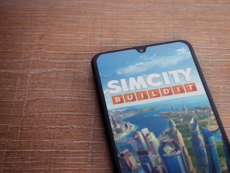Lod, Israel - July 16,2023: SimCity BuildIt app launch screen on smartphone on wooden background. Top view flat lay with copy space.