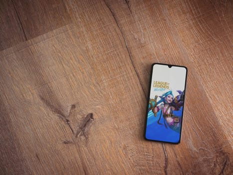 Lod, Israel - July 16,2023: League of Legends - Wild Rift app launch screen on smartphone on wooden background. Top view flat lay with copy space.