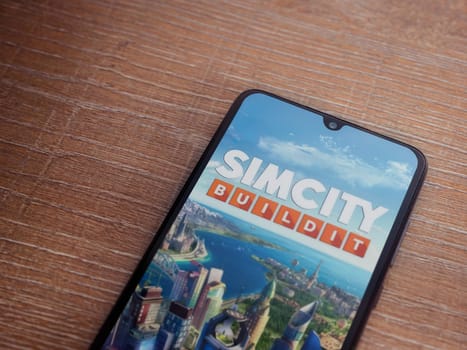 Lod, Israel - July 16,2023: SimCity BuildIt app launch screen on smartphone on wooden background. Top view flat lay with copy space.