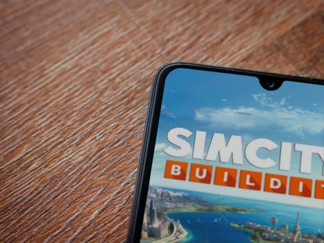 Lod, Israel - July 16,2023: SimCity BuildIt app launch screen on smartphone on wooden background. Top view flat lay with copy space.