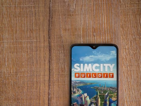 Lod, Israel - July 16,2023: SimCity BuildIt app launch screen on smartphone on wooden background. Top view flat lay with copy space.