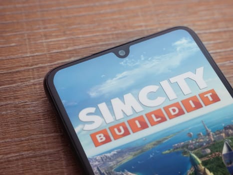Lod, Israel - July 16,2023: SimCity BuildIt app launch screen on smartphone on wooden background. Top view flat lay with copy space.