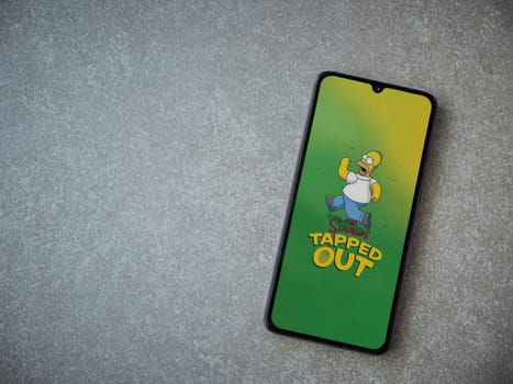 Lod, Israel - July 16,2023: The Simpsons Tapped Out app launch screen on smartphone on ceramic stone background. Top view flat lay with copy space.