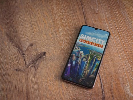 Lod, Israel - July 16,2023: SimCity BuildIt app launch screen on smartphone on wooden background. Top view flat lay with copy space.