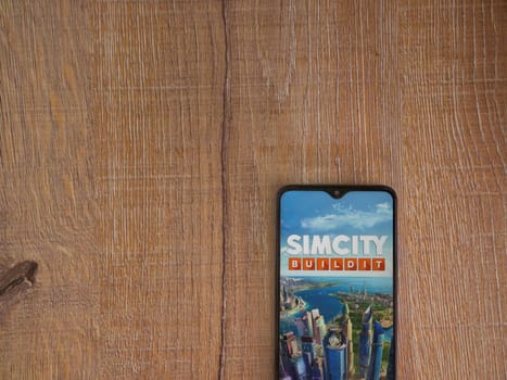 Lod, Israel - July 16,2023: SimCity BuildIt app launch screen on smartphone on wooden background. Top view flat lay with copy space.