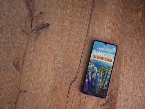 Lod, Israel - July 16,2023: SimCity BuildIt app launch screen on smartphone on wooden background. Top view flat lay with copy space.