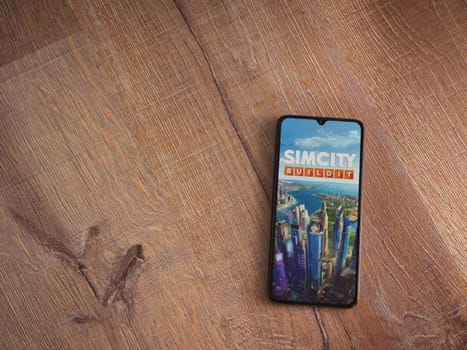Lod, Israel - July 16,2023: SimCity BuildIt app launch screen on smartphone on wooden background. Top view flat lay with copy space.