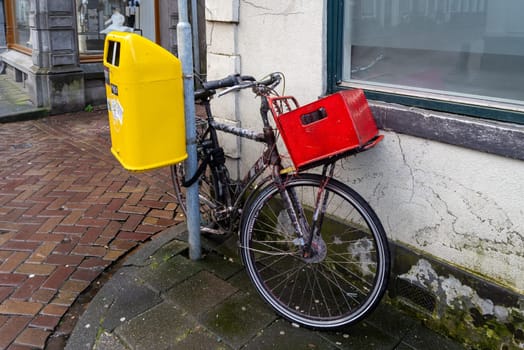 old bicycle with red basket parked next to a yellow dustbin