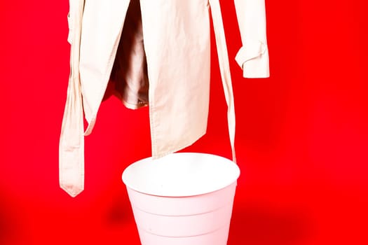 Shot of young woman hand throwing her outwear dress in the trash isolated on red background